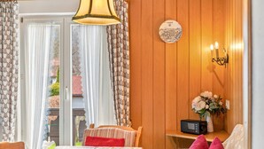Ein Zimmer mit einer holzgetäfelten Wand, einer runden Wanduhr, einem Radio, einer Vase mit Blumen und einem Tisch mit einer blumigen Tischdecke.