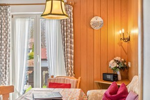 A room with a wooden paneled wall, a round wall clock, a radio, a vase with flowers, and a table with a floral tablecloth. - Apartment '1' with Mountain View, Shared Garden and Wi-Fi (Wallgau)