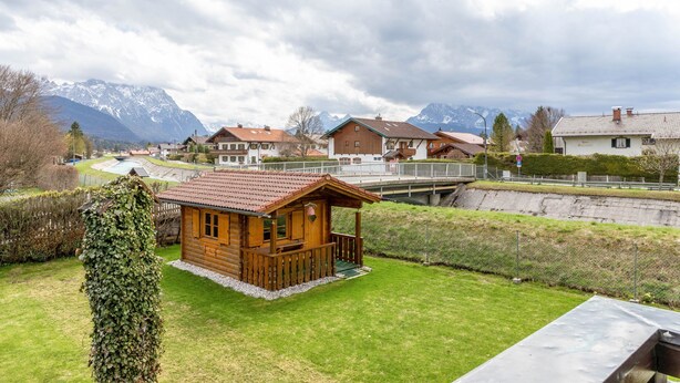 Eine Holzhütte mit Balkon, umgeben von einem gepflegten Rasen und einem Blick auf die Berge.