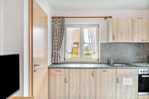 A kitchen with wooden cabinets, a stainless steel sink, and a window with curtains. - Apartment '1' with Mountain View, Shared Garden and Wi-Fi (Wallgau)