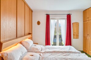 A bedroom with a wooden headboard, a bed with white bedding, a window with red curtains, and a wooden wardrobe. - Apartment '1' with Mountain View, Shared Garden and Wi-Fi (Wallgau)