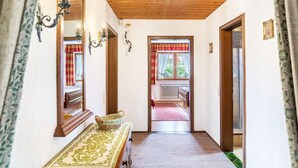 A hallway with a wooden ceiling, a mirror, a table with a basket, and a view into a room with a radiator and a window with curtains. - Apartment 'Parterre' with Mountain View, Private Terrace and Wi-Fi (Wallgau)