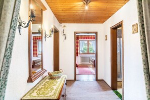 A hallway with a wooden ceiling, a mirror, a table with a basket, and a view into a room with a radiator and a window with curtains. - Apartment 'Parterre' with Mountain View, Private Terrace and Wi-Fi (Wallgau)