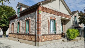 Un edificio de dos pisos con fachada de piedra, contraventanas verdes y un pequeño porche con barandillas blancas.