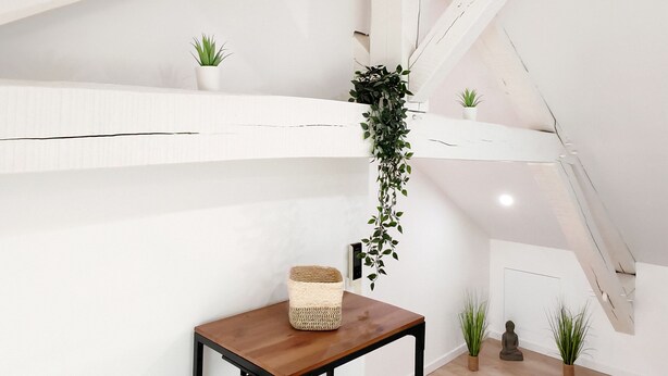 Una habitación con techo inclinado, paredes blancas y una mesa de madera con una cesta tejida.