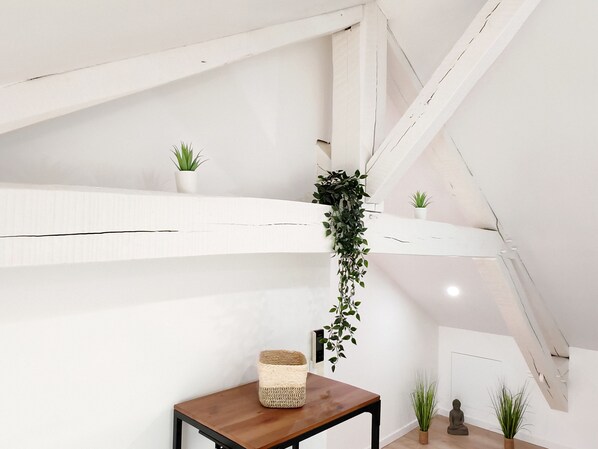 Une pièce avec un plafond en pente, des murs blancs et une table en bois sur laquelle se trouve un panier en osier.