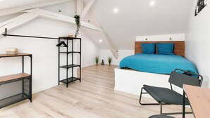 Un dormitorio tipo loft moderno con techo inclinado, cama con ropa de cama azul, escritorio y silla.