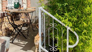 Un edificio de ladrillo con una puerta blanca, una pequeña mesa con sillas y un portón metálico que da a un jardín.