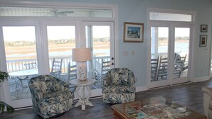 Una habitación con vistas a la playa, dos sillones con estampado, una mesa con lámpara y una mesita de centro con una revista.