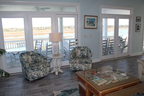 A room with a view of the beach, two patterned armchairs, a table with a lamp, and a coffee table with a magazine. - 7 Bedroom Across the Street from Beach / Access to Oceanfront Pool! (Ocean Isle Beach)
