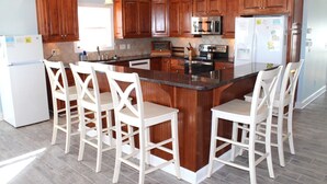 Una cocina con armarios de madera, una isla central con taburetes de bar, un refrigerador y un microondas.