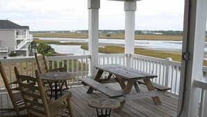 Una terraza de madera con mesas y sillas de picnic, con vista a un río y edificios distantes.