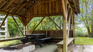 A rustic wooden pavilion with picnic tables and benches, surrounded by greenery. - House With Large Garden, Campfire hut 1 (Højer)