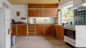 A kitchen with wooden cabinets, a white refrigerator, and an oven. - House With Large Garden, Campfire hut 1 (Højer)