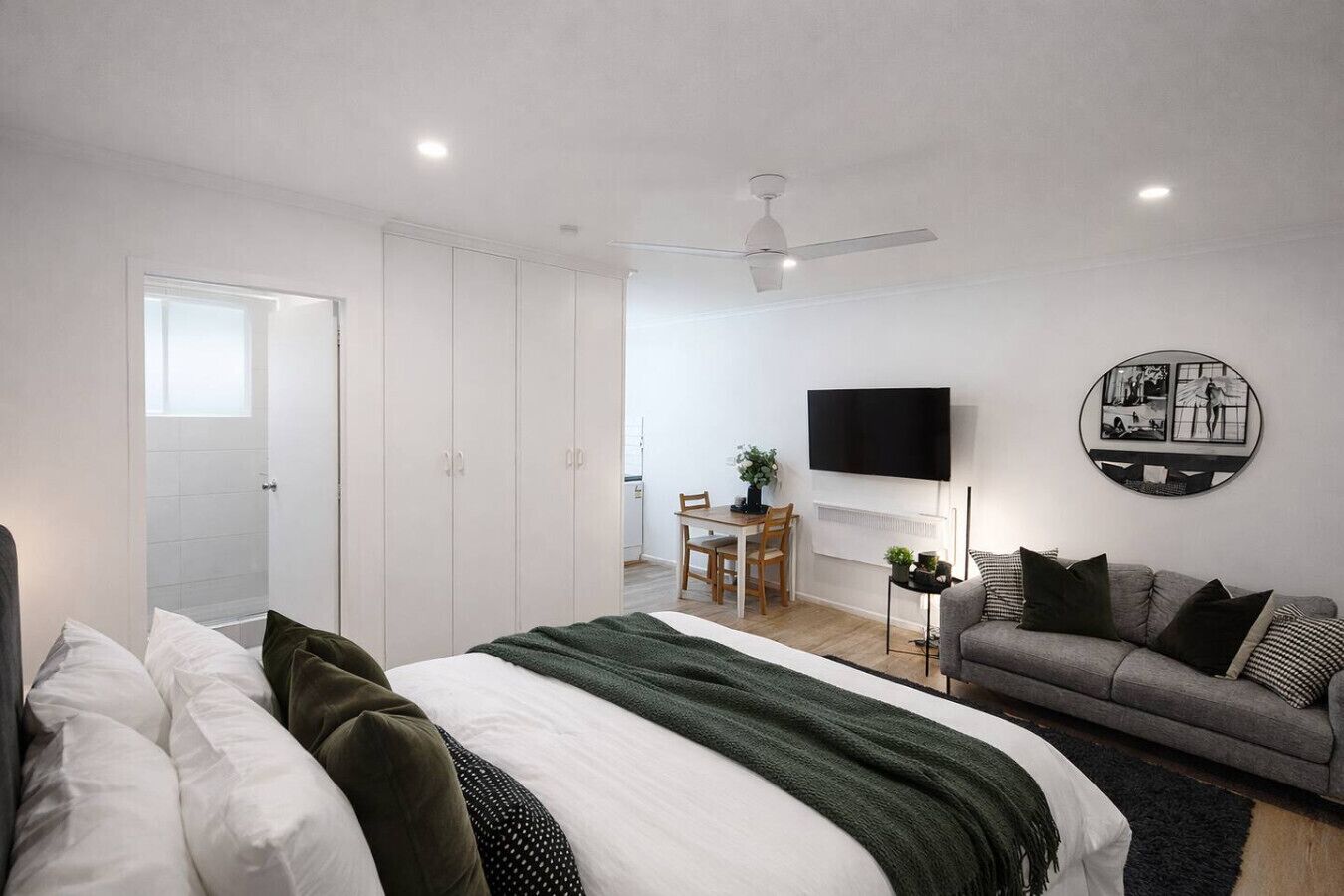 A modern bedroom with a bed, a sofa, a TV, and a dining area.