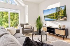 Ein stilvolles Wohnzimmer mit Sofa, Sessel und einem Fernseher, der eine Waldszene zeigt.