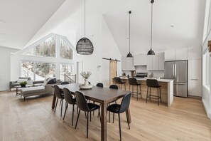 Eine moderne Küche mit einer zentralen Kochinsel, einem Essbereich mit großem Tisch und Stühlen sowie eine gemütliche Sitzecke mit Sofa und Couchtisch.