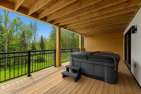 Une terrasse en bois avec un jacuzzi et un banc, offrant une vue sur un paysage verdoyant.
