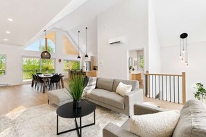 A spacious living area with a sofa, a coffee table, and a dining area with chairs and a table. - Chalet Mont-Tremblant | Spa - River - Game Room (Mont-Tremblant)