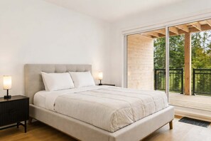 A bedroom with a large bed, two bedside tables, and a view of the outdoors through a sliding glass door. - Chalet Mont-Tremblant | Spa - River - Game Room (Mont-Tremblant)