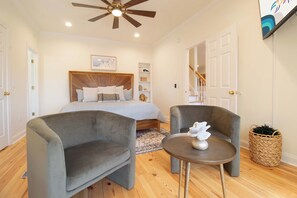 A bedroom with a bed, two armchairs, a small table, a ceiling fan, and a staircase. - Birdies and Beaches ~ relaxing golf retreat (Edisto Island)