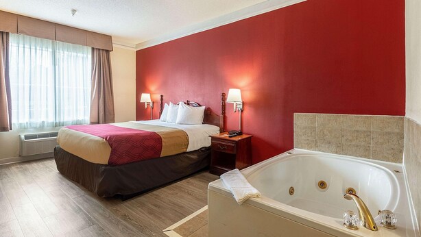 Ein Hotelzimmer mit einem großen Bett, einem separaten Badezimmer mit einer Badewanne und zwei Nachttischlampen.