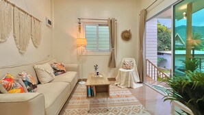 Ein Wohnzimmer mit einer Couch, einem Couchtisch, einem kleinen Tisch mit einer Lampe, einem Sessel und Blick auf Grünfläche.
