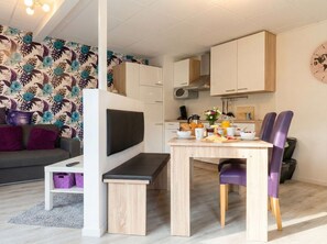 A compact living space with a kitchenette, a dining area with a table and chairs, a sofa, and a decorative wall.
