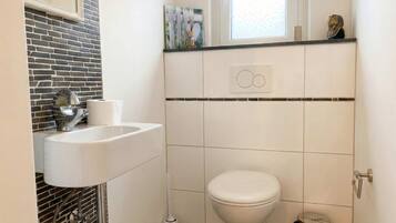 Un baño con un lavamanos blanco, un inodoro, una ventana y un pequeño cubo de basura.