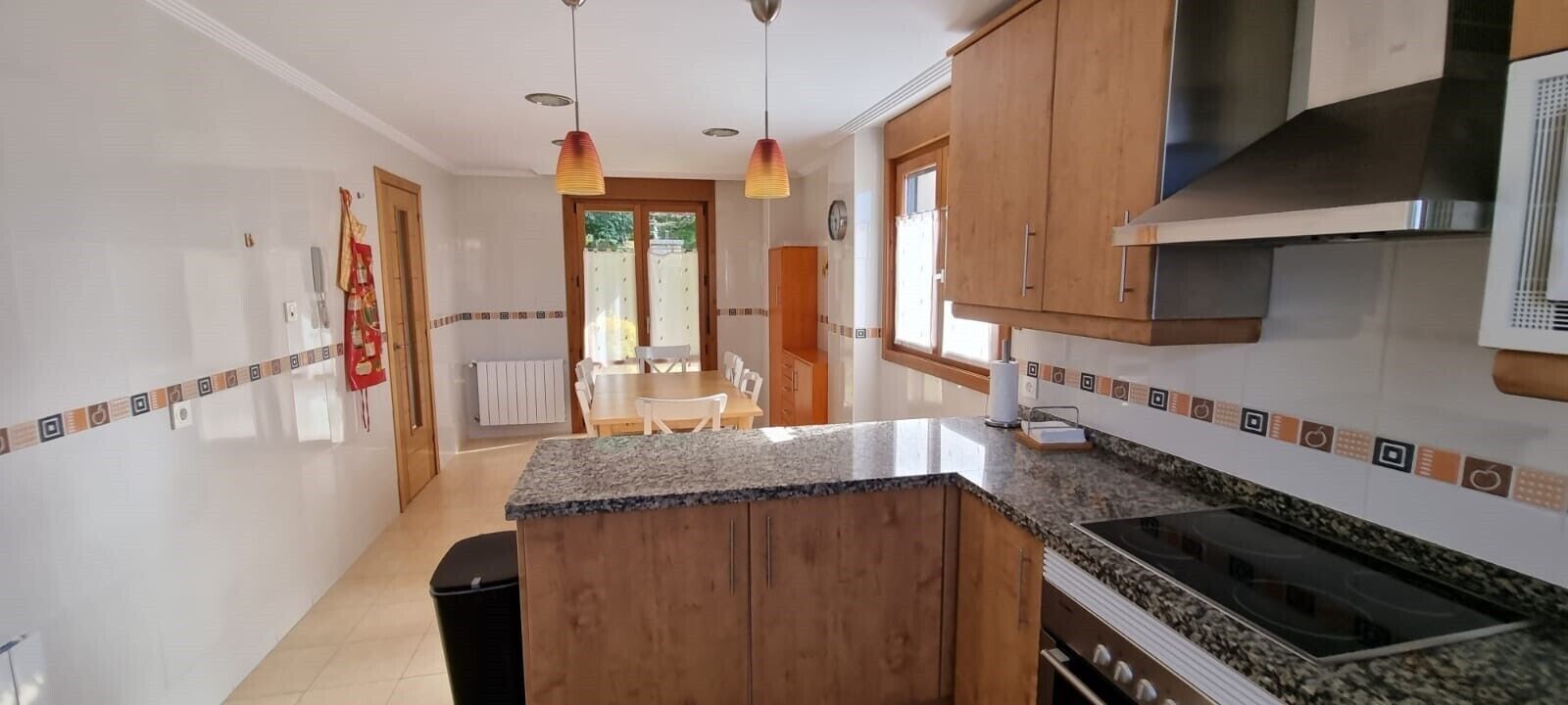 A kitchen with granite countertops, wooden cabinets, a built-in oven, and pendant lights.