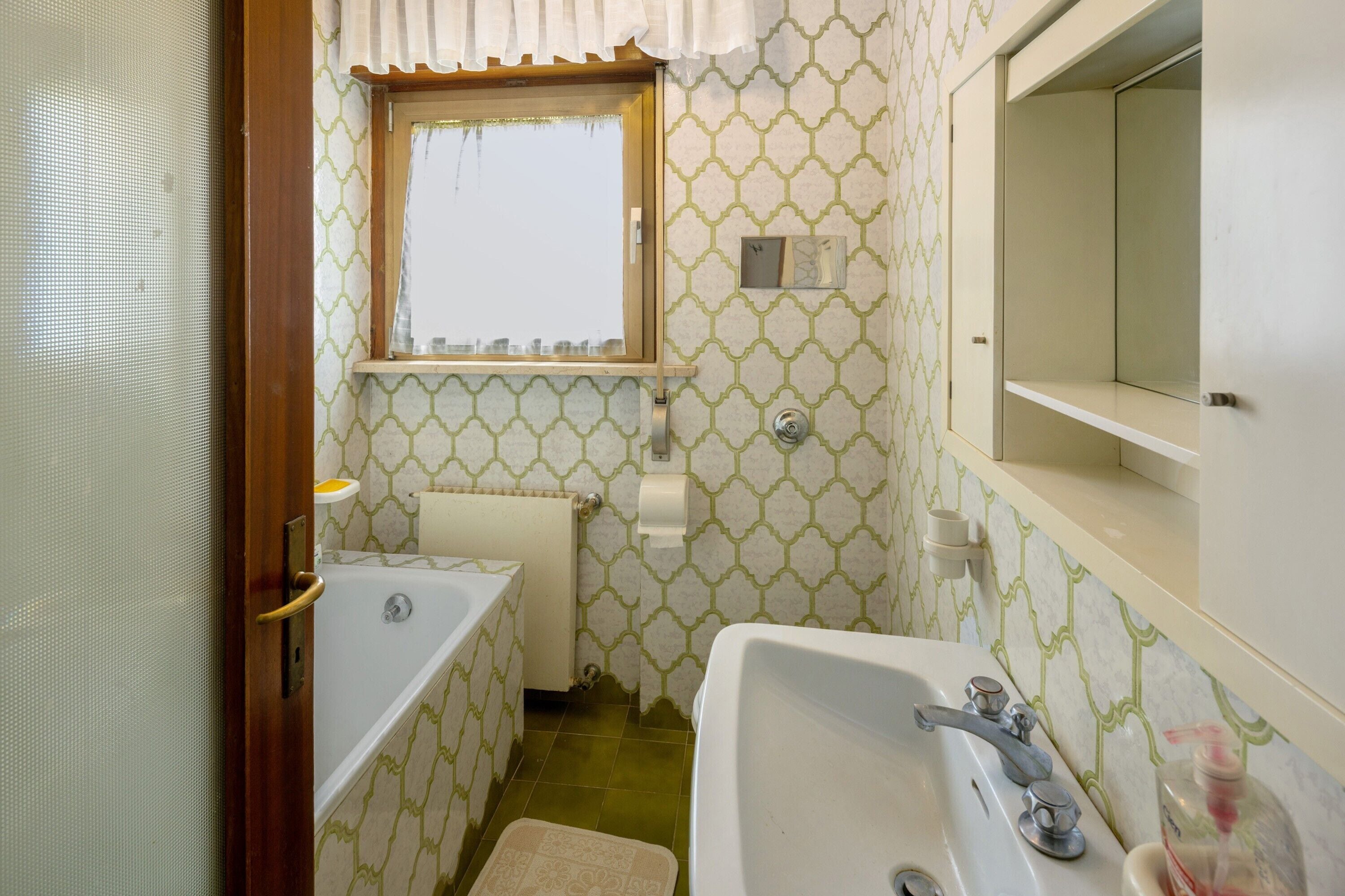 Une salle de bain avec une baignoire, un lavabo, une fenêtre et un papier peint à motifs.