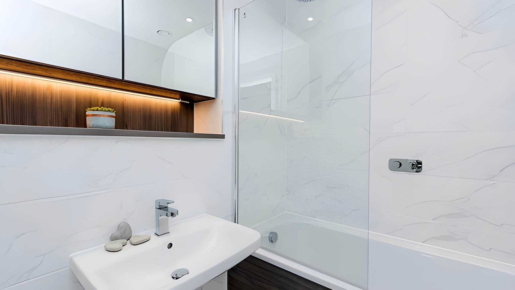A modern bathroom with a glass shower enclosure, a white sink, and a wooden vanity with a mirror.