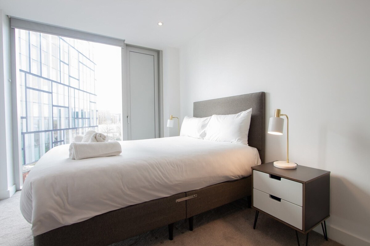 A modern bedroom with a large bed, bedside tables, and a view through a window.
