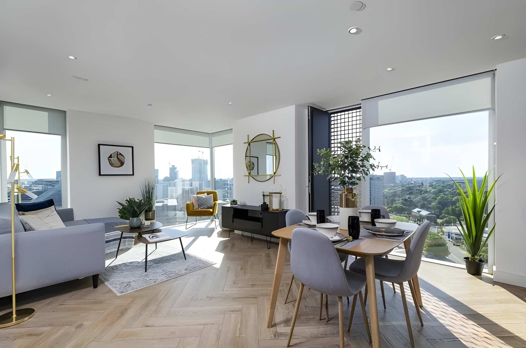 Un salon moderne avec un canapé, une table à manger et des chaises, de grandes fenêtres donnant sur la ville et une plante en pot.