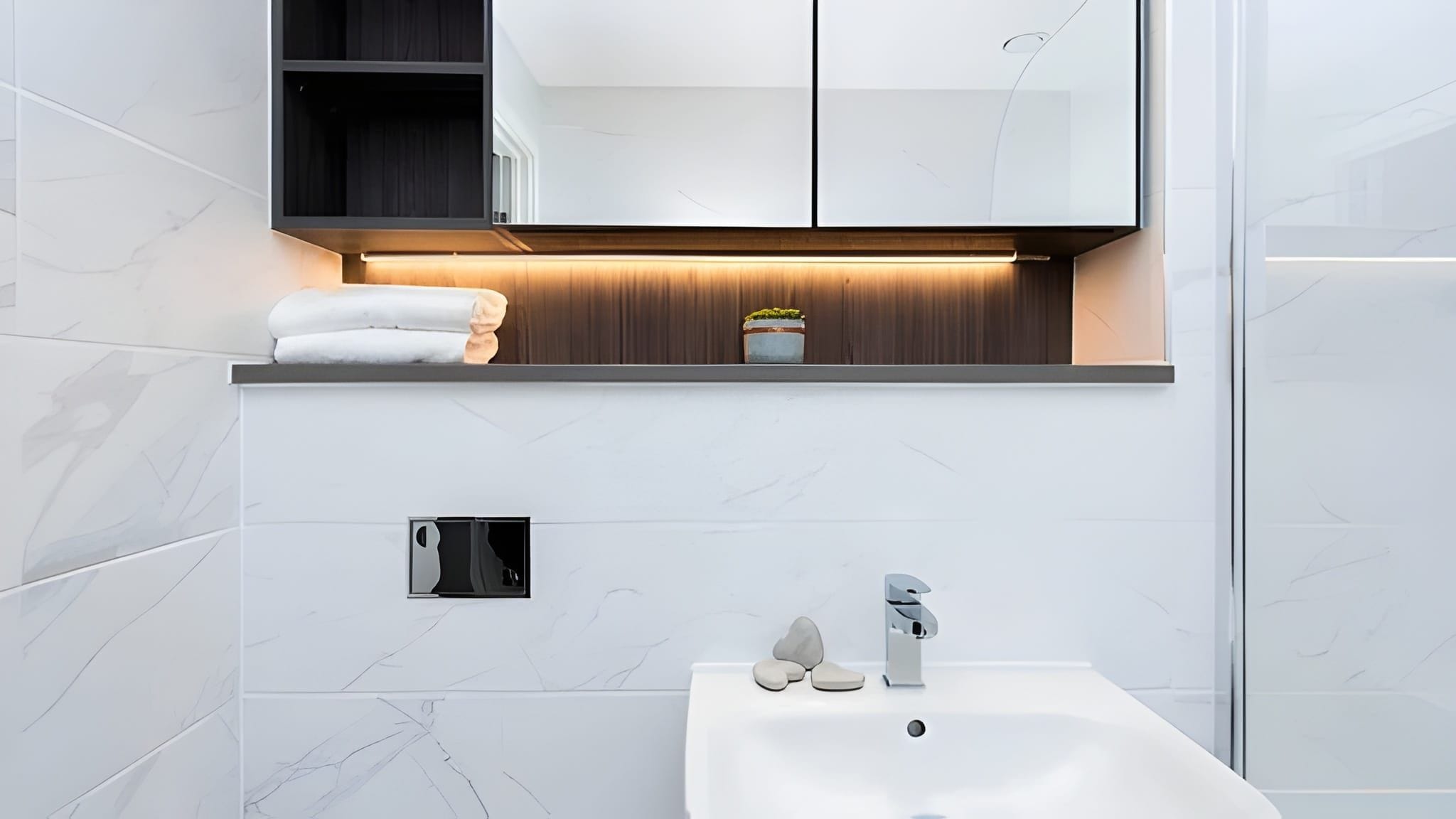 Un baño moderno con un lavabo blanco, un espejo y una repisa con una toalla y una planta.
