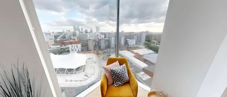 A modern room with a large window, a yellow chair, and a view of a cityscape.