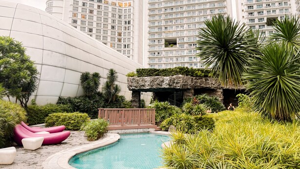 A modern building with a pool, surrounded by greenery and a small waterfall feature. - Cozy Retreat King Suite (Mandaluyong)
