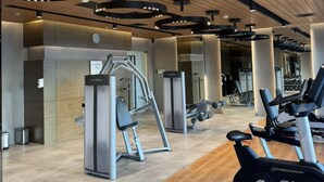 A modern gym with exercise equipment, wooden flooring, and a ceiling with circular light fixtures. - Cozy Retreat King Suite (Mandaluyong)