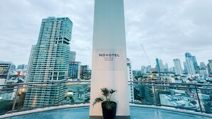 A modern hotel with a prominent column labeled 'NOVOTEL SUITES MANILA AT AQUA,' surrounded by a cityscape with high-rise buildings and a construction crane. - Cozy Retreat King Suite (Mandaluyong)