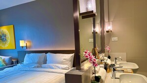 A hotel room with a bed, a bathroom with a sink and mirror, and a wall-mounted light fixture. - Cozy Retreat King Suite (Mandaluyong)
