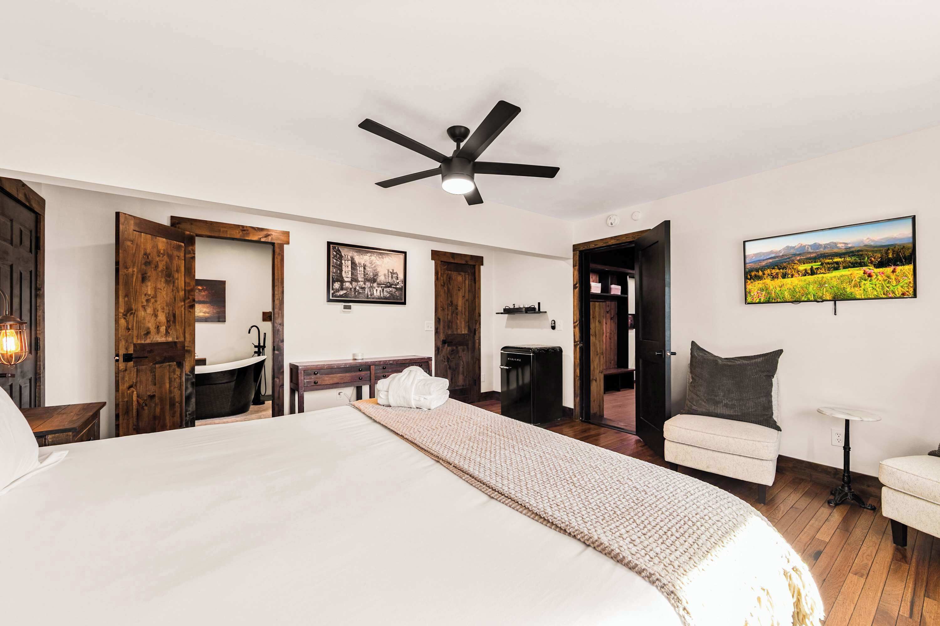Ein Schlafzimmer mit einem großen Bett, einem Deckenventilator, einem Badezimmer mit einer Badewanne und einem Gemälde an der Wand.