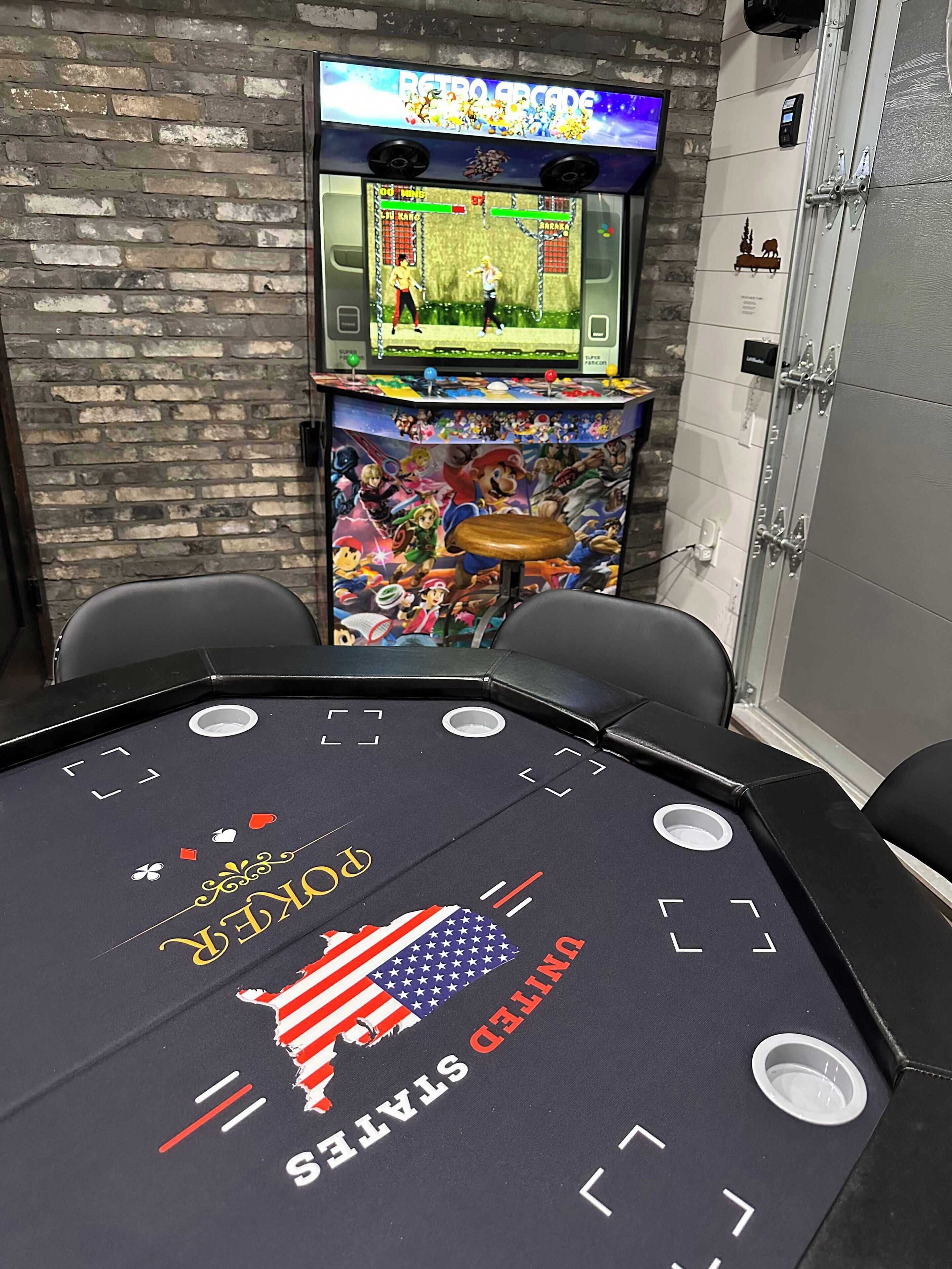 Uma área de jogos com um fliperama retrô, uma mesa de centro com o desenho da bandeira dos EUA e uma parede de tijolos.