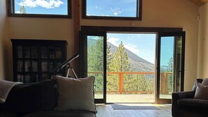 Una habitació àmplia amb un sostre alt, un ventilador de sostre, una finestra gran i vista a una muntanya.