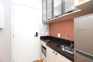 Eine kleine Küche mit integriertem Backofen, einer Spüle aus Edelstahl und einem Kühlschrank.