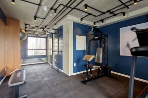 Ein Fitnessraum mit Trainingsgeräten, Laufband und Fenster mit Blick auf die Stadt.