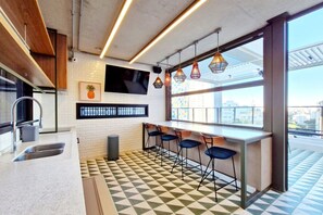 A modern kitchen with a checkered floor, bar stools, a TV, and a large window with a city view. - Blend (São Paulo)