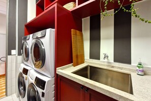 A laundry area with stacked washing machines, a wooden drying rack, a sink, and a bottle of hand soap. - Blend (São Paulo)