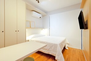 A bedroom with a bed, a desk, a wardrobe, an air conditioning unit, and a television. - Blend (São Paulo)