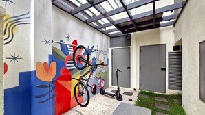 A covered outdoor area with a colorful mural, a bicycle, a tricycle, and a scooter. - Blend (São Paulo)