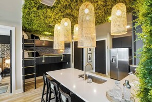 A modern kitchen with a central island, black and white cabinetry, and a green wall with foliage. - Bourbon & Broadway - Luxury Living 1.3 miles to Broadway, Brand New, 6 Beds! (Nashville)